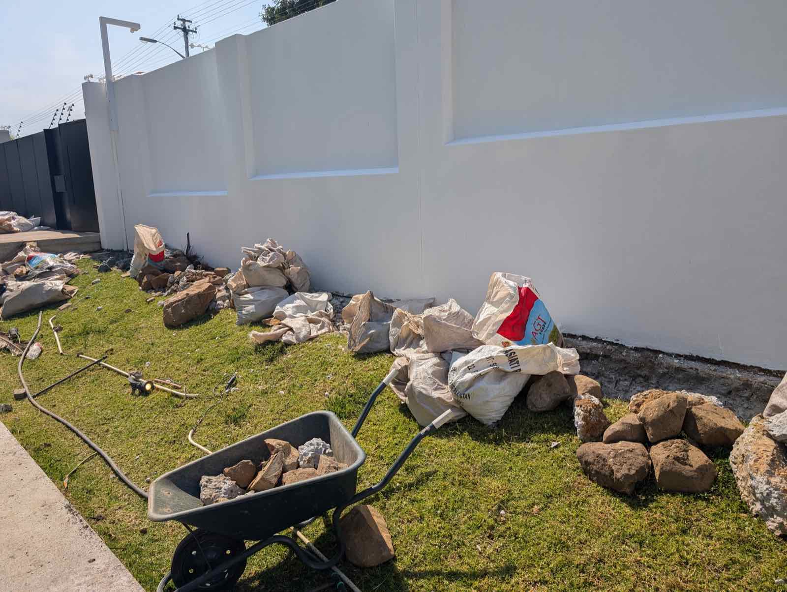 Wheelbarrow of rocks and rubble strewn across the lawn against a freshly painted wall