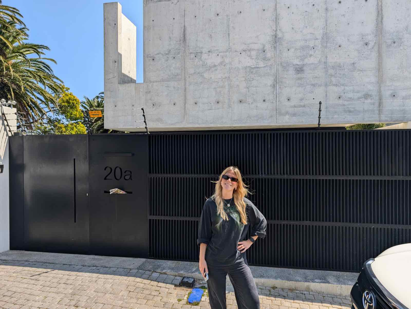 Kira standing at the 20A gate in front of the raw concrete facade